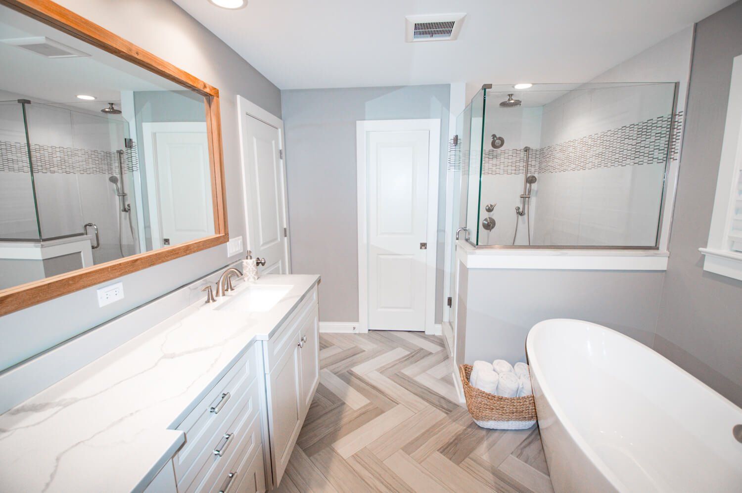 Bright primary bathroom remodel with a freestanding tub, glass shower, double vanity, and herringbone floor