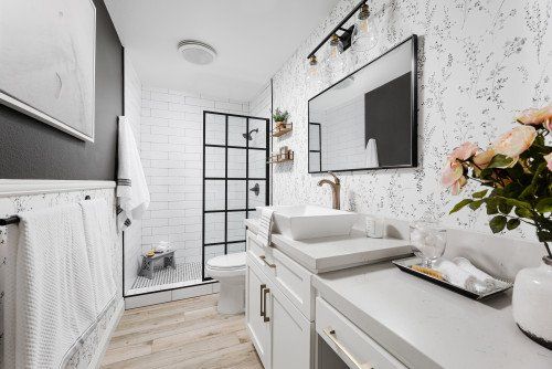 Compact bathroom remodel with a white vanity, black framed shower door, and patterned wall finish