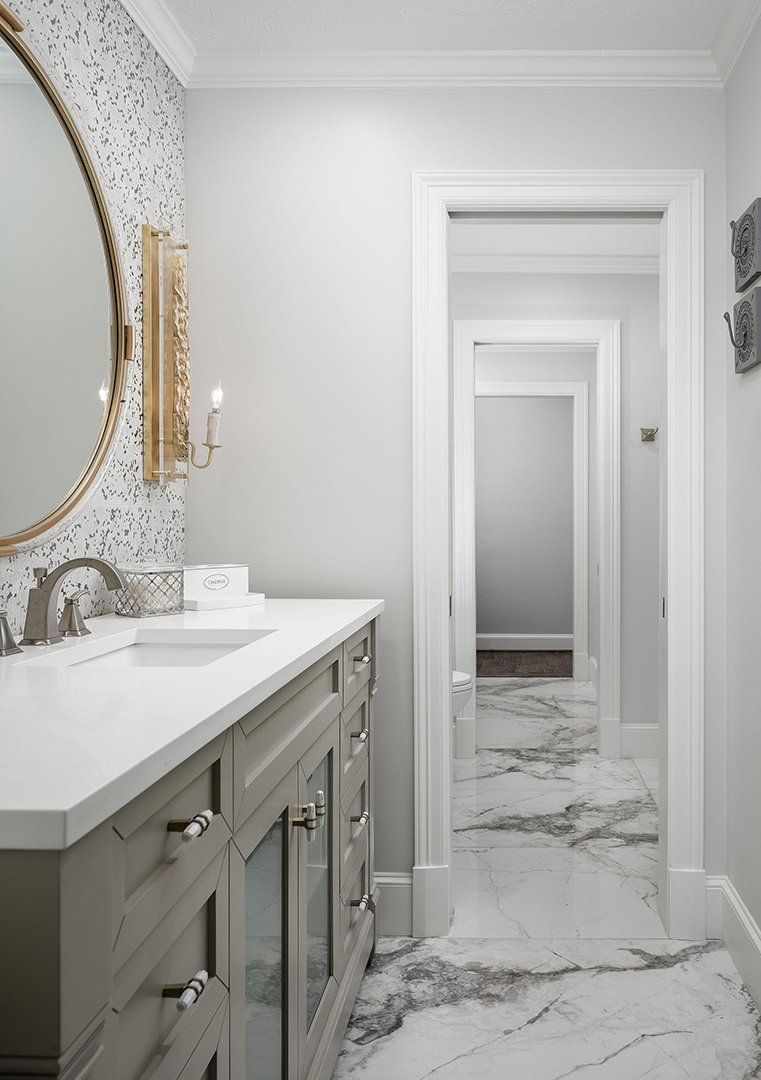 Custom bathroom remodel with a long double vanity, round mirror, wall sconces, and marble-look floor