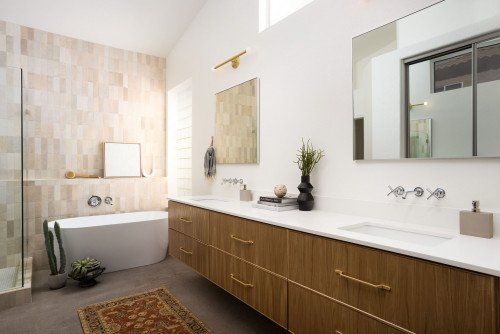 Warm primary bathroom remodel with a wood vanity, soaking tub, glass shower, and brass fixtures